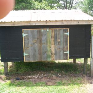This view shows the clean out doors. I made frames for the doors out of wood I salvaged from an old box spring. I nailed slats from pallets on the outside with tar paper underneath. Then I turned it over and put half inch foam insulation inside the frame then 1/8 inch plywood from crates I got from work . Top left is my finger.