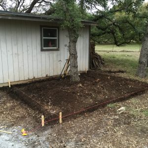 We started by measuring out and trenching right next to the tool shed.  This would be the ideal place to build the coop and run, as it was within viewing distance from the back windows of the house.  The footprint ended up being around 12' x 14'.  We dug about 10" into hard Texas black clay to make room for the cinder blocks that would go in for the foundation.  Notice that we intentionally left the oak tree running right through the middle of the run area.