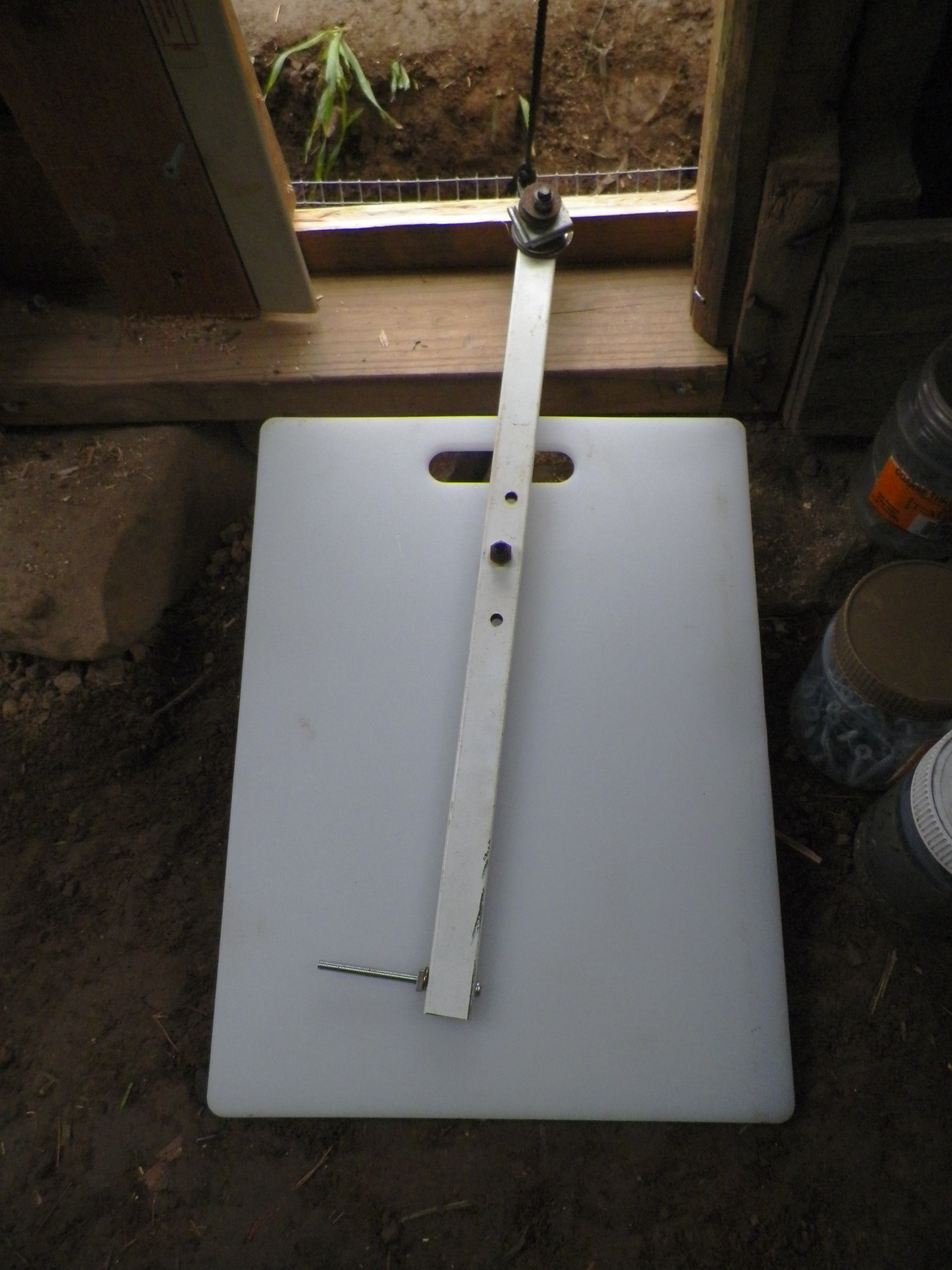 Self latching chicken door made of a cutting board. Swing arm of metal part from an EZ-up frame. This is significant to us, as we are full time crafts people and the folding tent covers are a big part of our lives. Counter weights of washers, and bolt pin.
