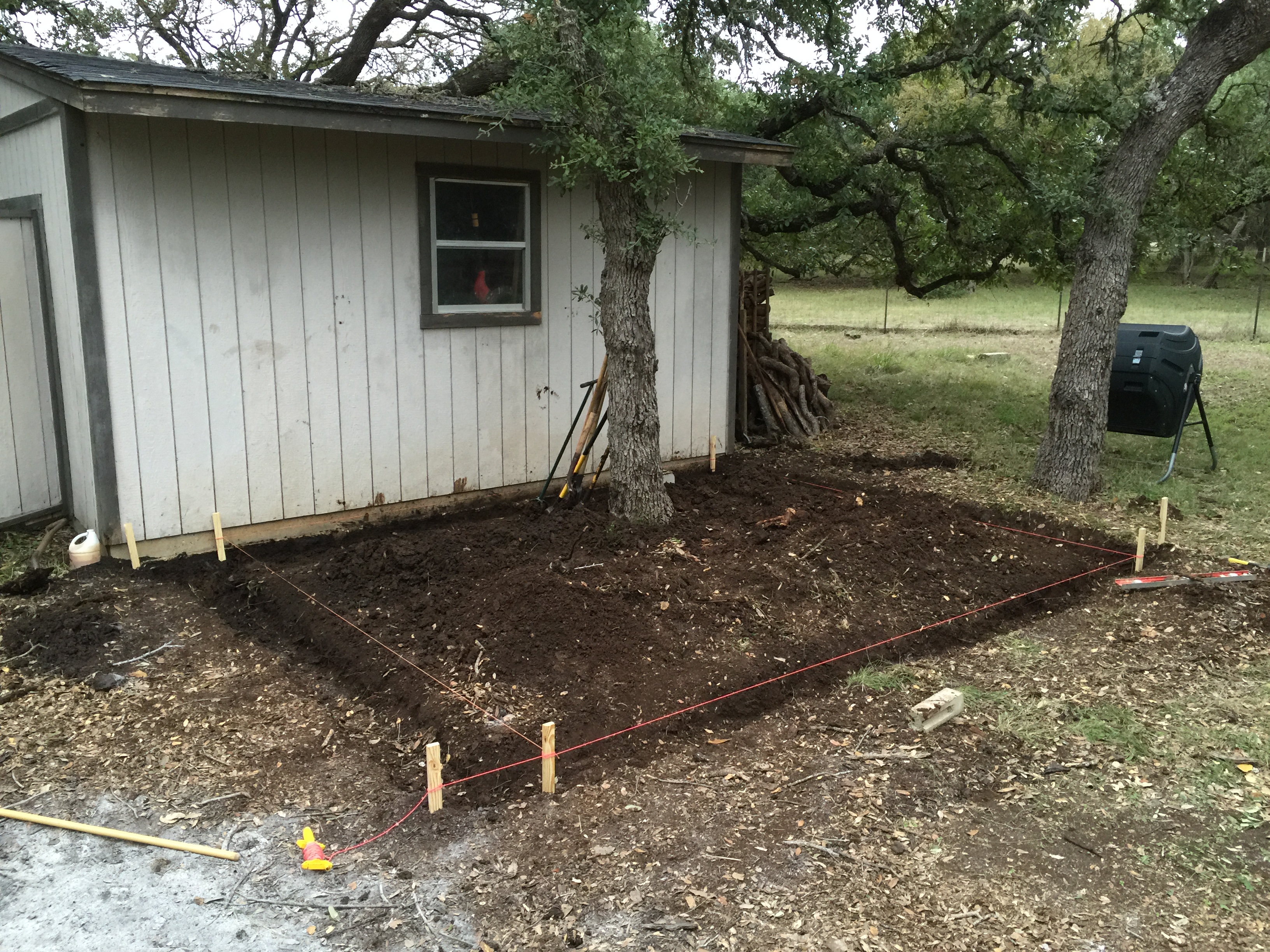 We started by measuring out and trenching right next to the tool shed.  This would be the ideal place to build the coop and run, as it was within viewing distance from the back windows of the house.  The footprint ended up being around 12' x 14'.  We dug about 10" into hard Texas black clay to make room for the cinder blocks that would go in for the foundation.  Notice that we intentionally left the oak tree running right through the middle of the run area.