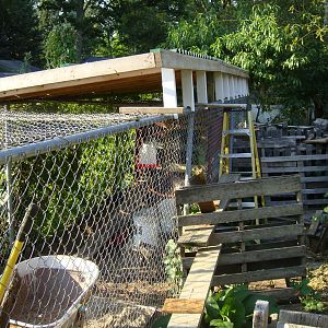 The 2 x 4 " pcs were added  (bolted) to the roofing sections we constructed in the driveway. They are the white vertical pcs about 18 " long holding the east side of the roof up. Note rounded bottom  cut out of The "risers" to fit around the pipe framework of the fencing.. Also see the pallates used as part of some scaffolding helpful in working on roof.  [ If used, be sure lumber is strong enough and fastened together solidly enough to support your wweight.... I didn't do that. ] OUCH ... Only hurt for a little while.