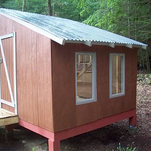 Back view of coop.  Instead of shingles, we opted for the smoke panels that let in lots of light.  So far it hasnt gotten too hot in there.  The windows are there for more light.  In the book, woods has this wall as solid.  We wanted as much light as possible because there is no electric in it.  The door is custom, smaller than a regular door and you step down onto the coop floor.