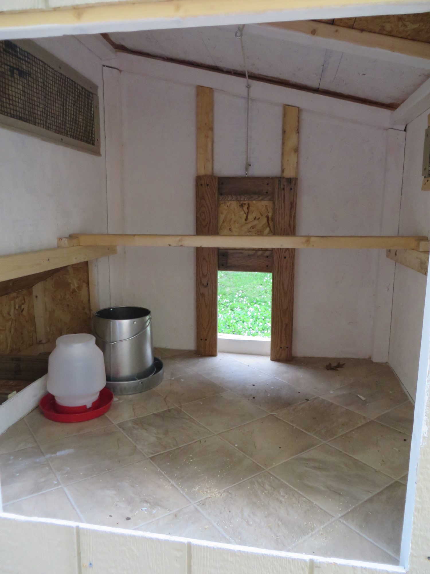 An early look inside the coop. The pop door is on a pulley that runs along the ceiling and is operated from the large cleanout door. The food and water currently are kept in the run, but I will probably hang them in the coop during the winter.