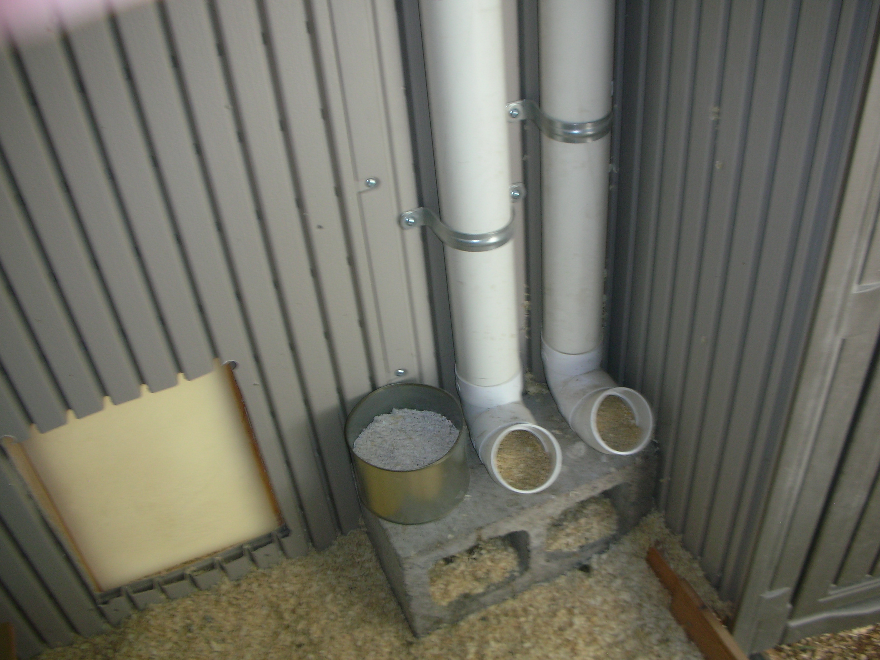 Here's the feed station right next to the pop hole (notice the bottom cut of the pophole? A tad "curvy" .. that sword saw thingie scared me to death! Anyways, 2 PVC tube feeders, oyster shell to the side, all on a cinder block.