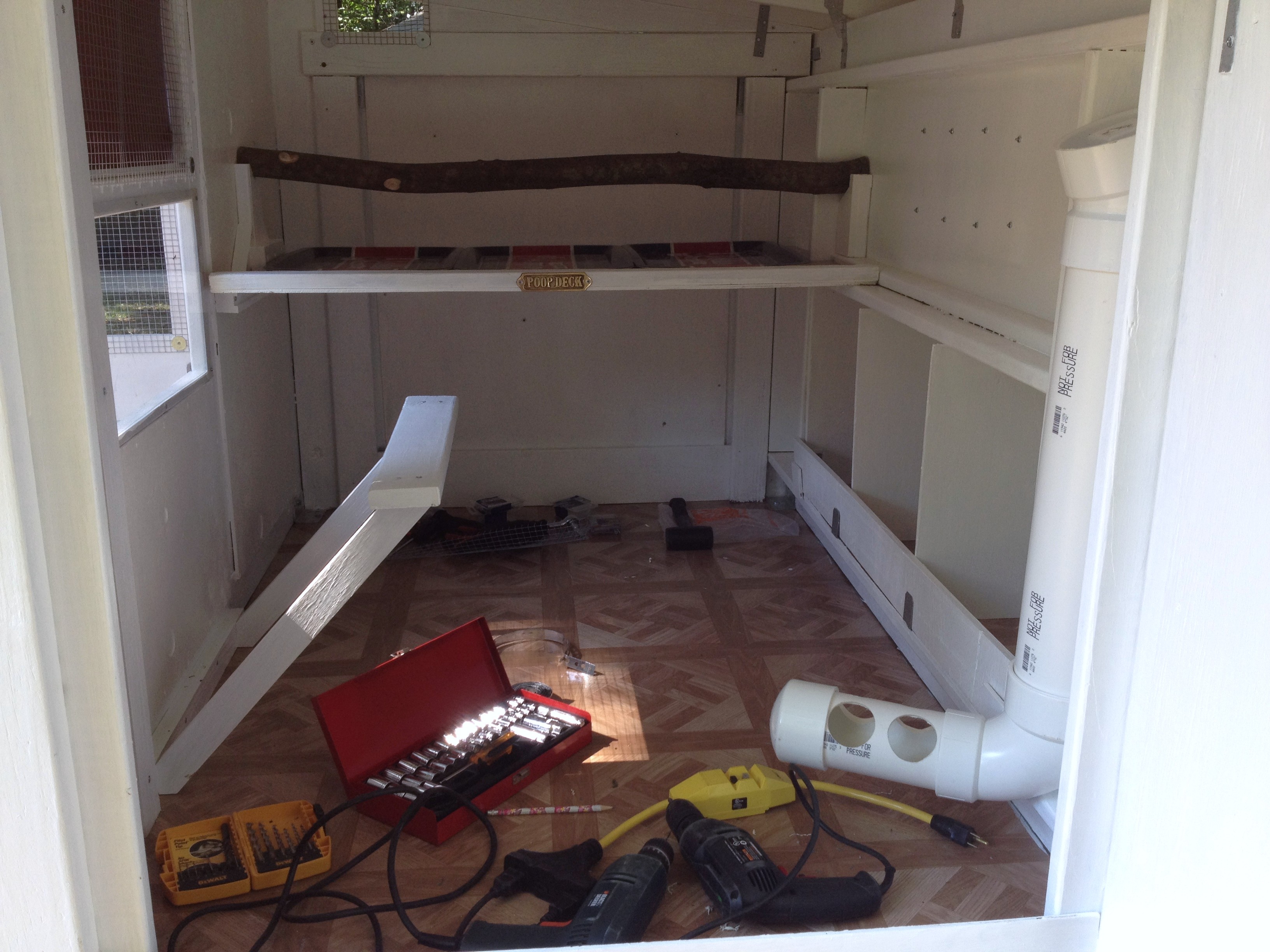 Inside of coop - roosting bar with poop deck in center, nesting boxes on right along with PVC feeder