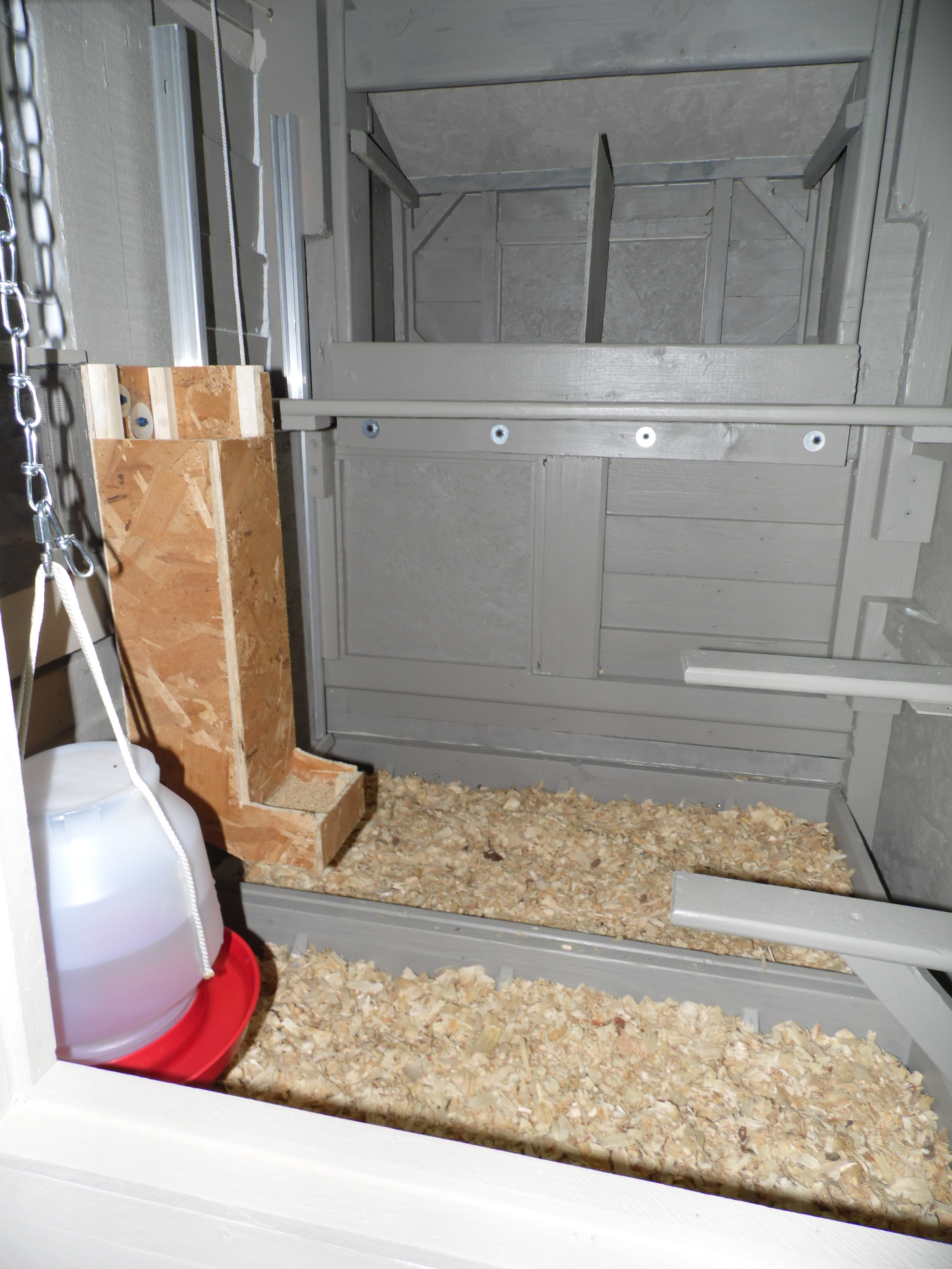 Inside of our coop. The hanging water idea came from a fellow backyard chicken member (don't remember who, but THANK YOU)! Hot glued string to it and used chain so as chickens grow I can raise it. The feeder I made: simple 1/4 inch OSB with small cleats inside to hold together. Works good and they don't waste near as much food! The top roost is removable. The door to the run is simple: eye lags with string to outside to raise and lower. And the saw chip trays: 2 trays that can be easily removed, dumped and put back. Underneath the trays I attached hardware cloth so chickens don't fall through while you dump.
