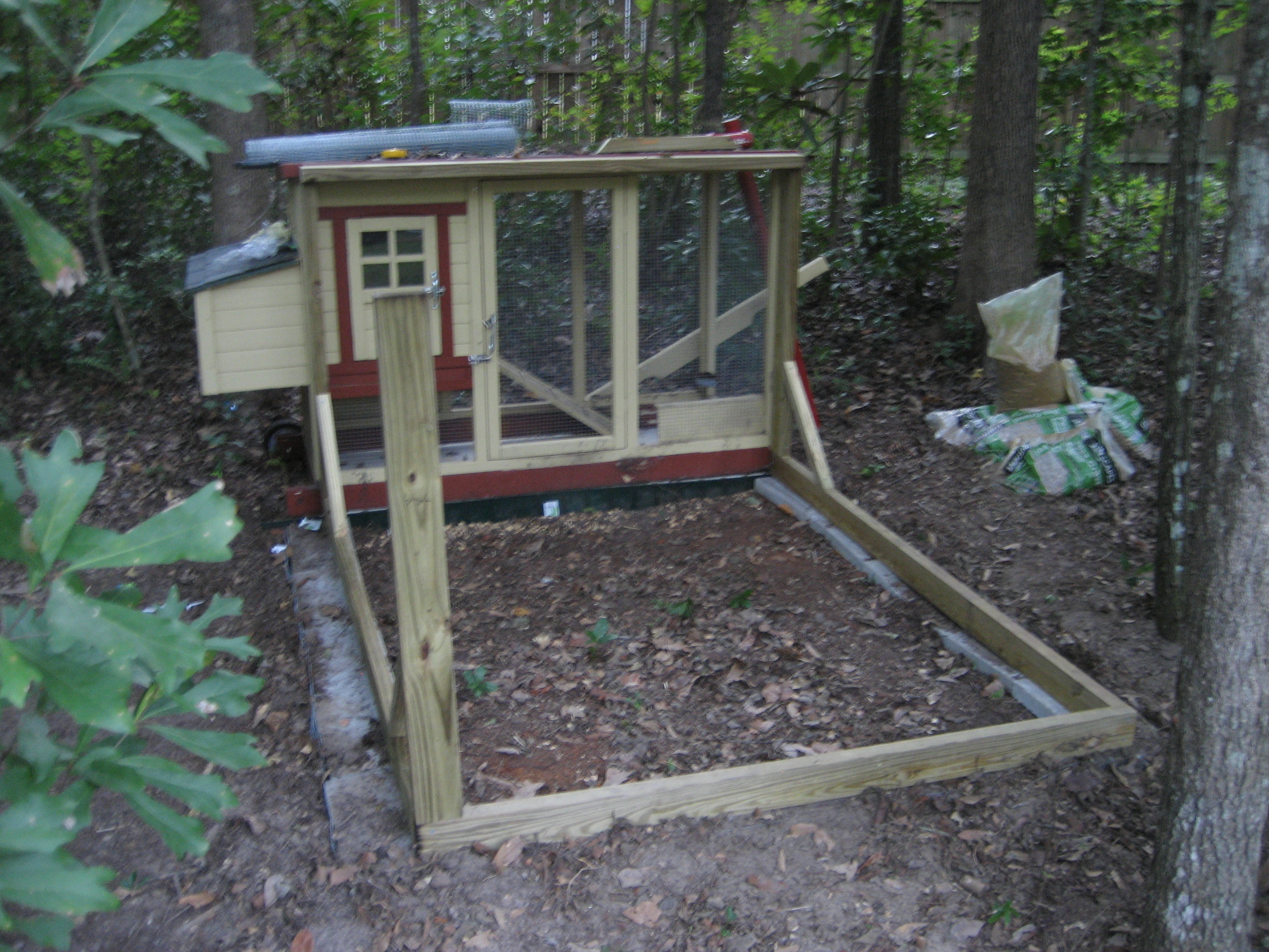 My clever brother is responsible for this design. First we removed the left arm of the tractor and both wheels. We placed the main coop on pavers. We prepped the ground by digging a bit down, the put river rocks down for drainage. Then pavers, then the coop. Between coop and run area, more rocks, and then landscaping edging between the coop and the new run. 
We dug down just over 1 foot all the way around the front of the frame, and buried 1 ft of hardware cloth. That was HARD! Outlined with pavers, more river rocks, then he put in the frame. 

***I'm calling them pavers which is not what they are. They are cement blocks, but the little top sections. Basically the top of a cement block. Sorry for the 'girl' description, I'm out of my realm of expertise here.