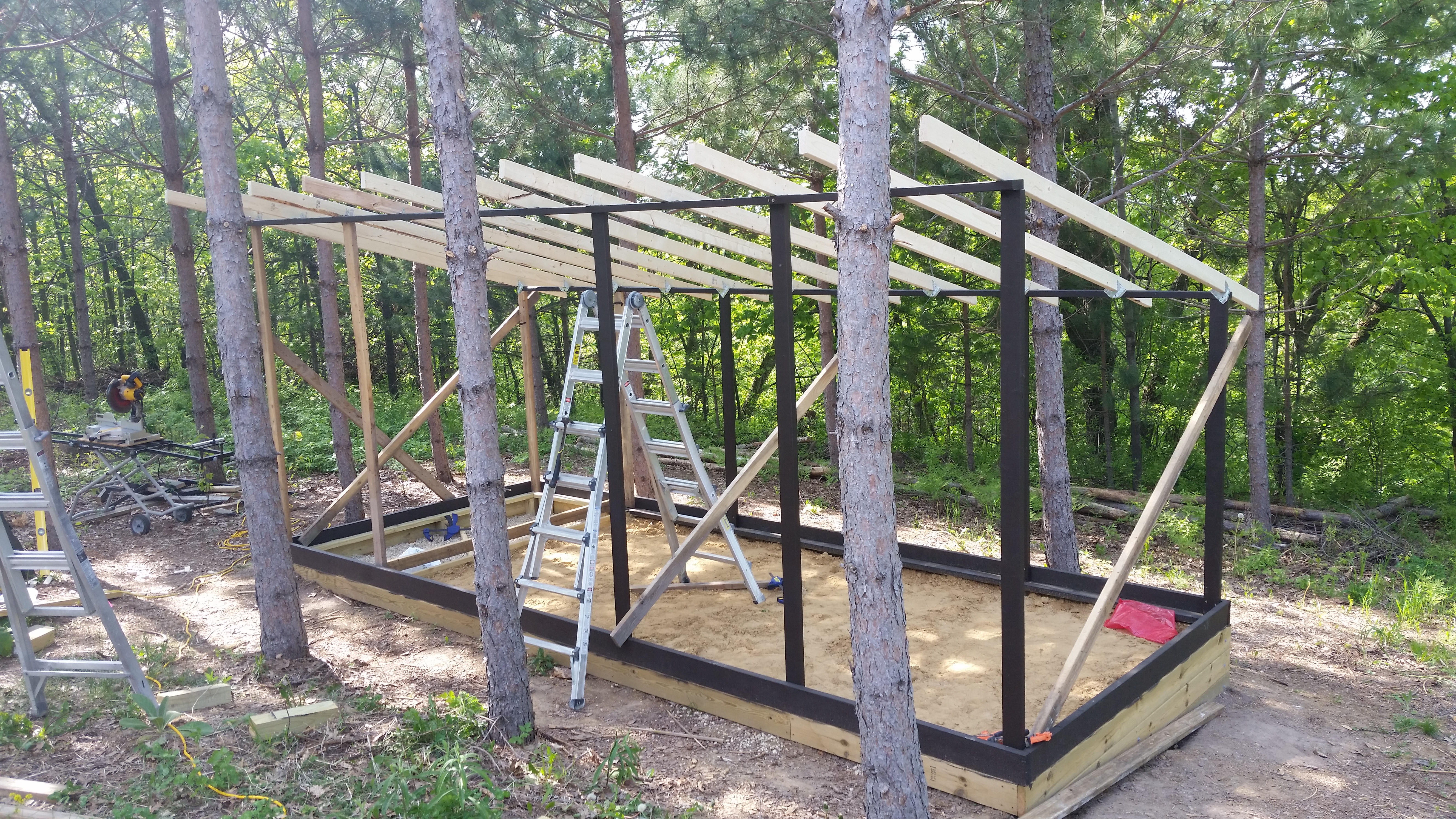 Setting the initial bracing and roof trusses.  The uprights are four feet on center.  This allowed easy access as the build progressed.  After the structure was largely completed, the remaining uprights were added at twenty four inches on center, and doubled up for strength.