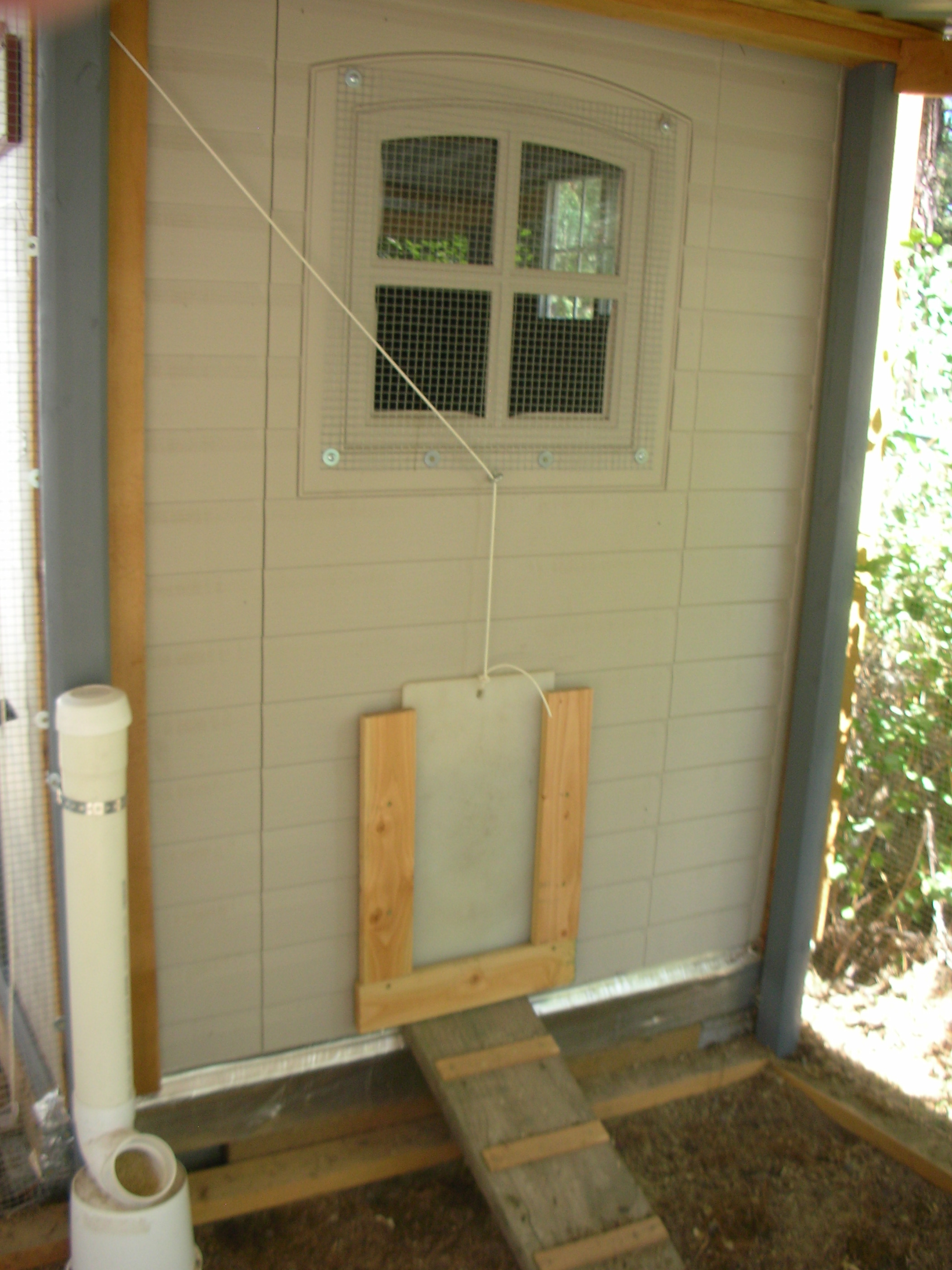 That window came with the shed, it does open up and down. 1/2" hardware cloth over it, and there's the infamous pophole, what a job that was for me using that sword saw thingie. It's a good thing the wood slider setup covers up the wavy cuts!! I used an old cutting board, cut it to size, and drilled a hole in the top for the cord.