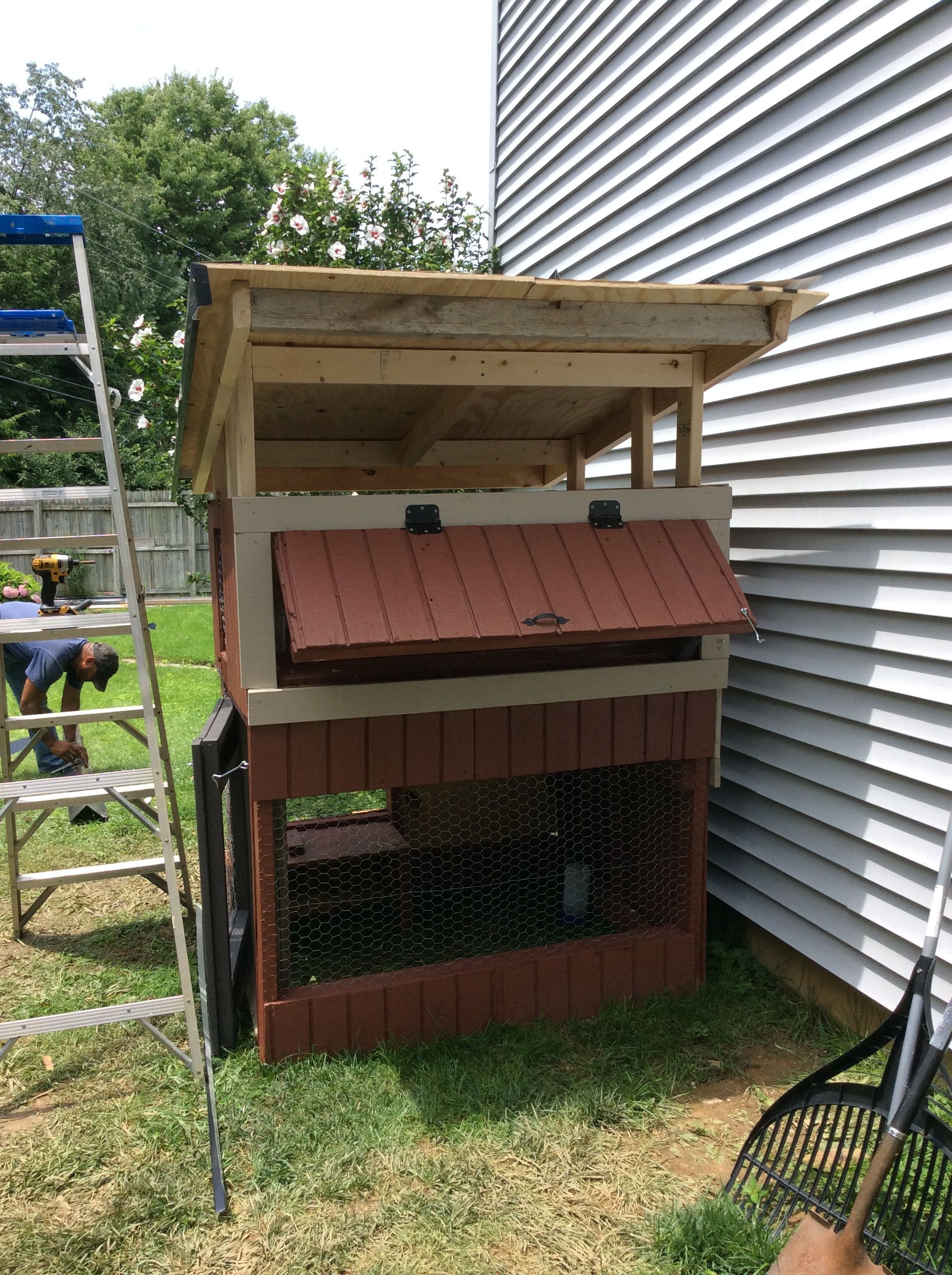 The installation of the metal roof was the only part of the coop that I needed help with. I employed one of the roofers who installed the roof on my house, a few years ago, to snip the metal and help me attach it to the structure. He also installed the gutter and spout. I went with a lean-to style roof because of the limited material I had for a gutter and spout, and I wanted more control of the water run-off direction. 

By the time Andre came over to help me with the roof, I had pretty much all of the rest of the outside completed. In this photo the hinged, nest door is shown propped open. Later, I cut a 1X1 and attached a repurposed piece of industrial-like cord to one end of the 1X1, while attaching the other end of the cord to the inside of the nest. That way, the 1X1 pole won't get lost or misplaced.